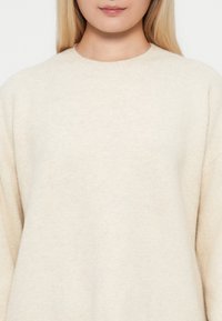 Maglione color crema con una texture morbida, scollo rotondo e spalle scese, caratterizzato da un design semplice e minimalista.