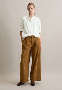 Witte button-up shirt met een kraag en opgerolde mouwen, in combinatie met bruine wijde corduroy broek, staande op bruine laarzen.