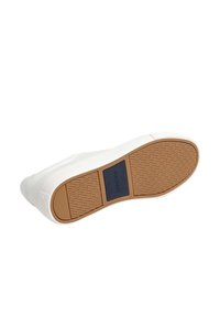 Zapatilla blanca con suela de goma texturizada, detalles en color marrón y parche de logo negro. Superficie superior lisa con detalles de costura.