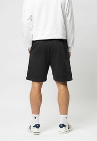 Zwarte zwembroekshorts met een trekkoord in de taille, zijzakken en een relaxed fit, gecombineerd met een witte lange mouw top en sneakers.