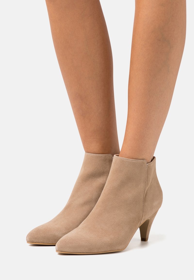 Beige ruskind ankelstøvler med spids tå og lav hæl. Glat tekstur og minimalistisk design med en buet silhuet.