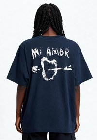 T-shirt surdimensionné bleu marine en coton, avec le texte graphique blanc "Mi Amor" et un motif de flèche au dos. Manches courtes, coupe décontractée.