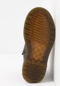 Suola di scarpa marrone con un motivo di grip testurizzato, caratterizzata da un materiale semi-trasparente e linee di battistrada prominenti. Design della punta arrotondata.