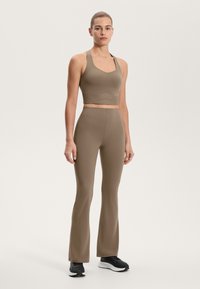 Rjav rebrast športni modrček in hlače z visokim pasom in širokimi nogavicami. Gladka tekstura, prilegajoča zasnova, s kontrastno poudarjeno črno obutvijo.