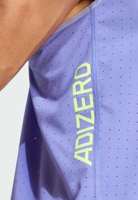Top deportivo atlético morado con pequeñas perforaciones, que presenta un logo vertical en neón amarillo "ADIZERO" en el lateral y costuras contrastantes.