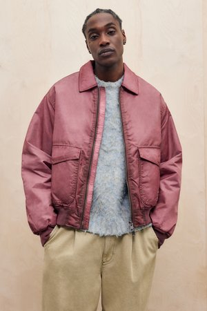 Maroon bomber jacket with large front pockets, paired with a fuzzy blue sweater and beige trousers. Smooth texture and relaxed fit.