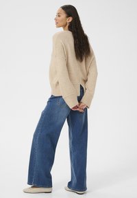 Maglione beige a maglia con maniche ampie, abbinato a jeans blu a vita alta e larghi. Palette di colori sobria e neutra e silhouette rilassata.