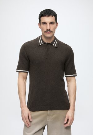 Uomo con capelli corti e baffi che indossa una polo marrone scuro a maniche corte con trama e righe bianche su collo e maniche.