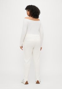 Hvit off-the-shoulder langermet topp paret med hvite joggebukser med elastisk midje, som har to baklommer og teksturerte sneakers.