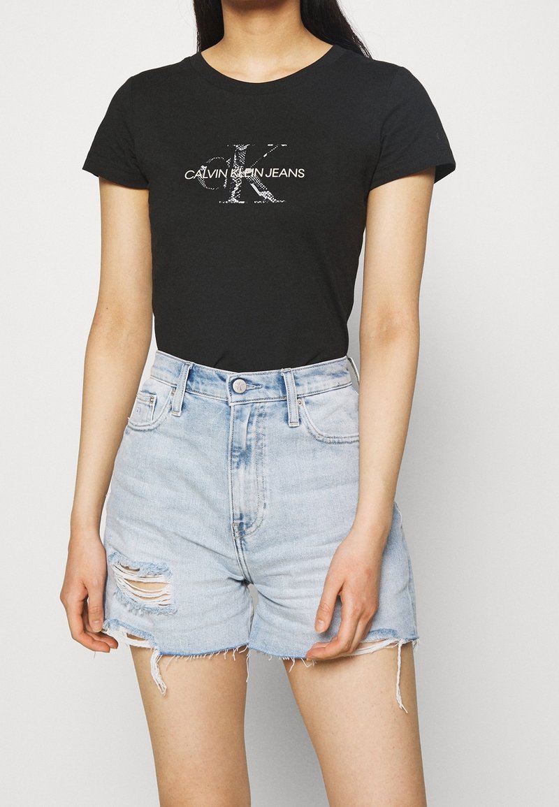 Czarny bawełniany t-shirt z białym logo "CALVIN KLEIN JEANS". Połączony z jasnoniebieskimi szortami dżinsowymi z postrzępionym dołem i przetarciami.