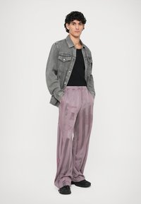 Pelēku denimu jakas virs melnas kreklas, apvienotas ar brīvā griezuma, gaiši purpura biksēm ar vertikālām svītrām un grafiskām apdrukām. Melna apavu.