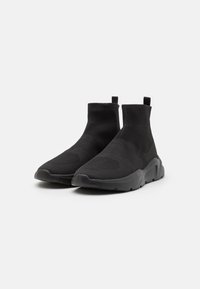 Black knit ankle boots with a textured upper, elastic sock-like collar, and a chunky sole featuring a patterned tread. Durable and flexible design.
