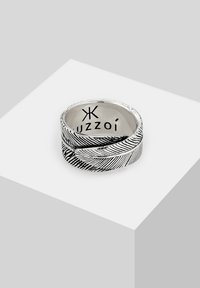 Silverfärgad ring med ett lövdesign med ingraverade detaljer och en polerad yta. Insidan är märkt med varumärket "Uzzoi."