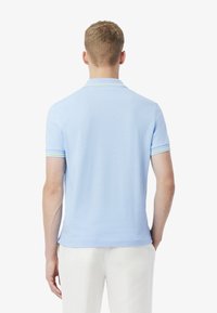 Ljusblå piké med korta ärmar, utrustad med kontrasterande gröna och vita ränder på kragen och ärmsluten. Minimalistisk design.