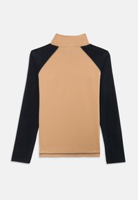 Pull-over en polaire avec un col montant, présentant une devant beige et des manches noires. Texture lisse avec des coutures visibles le long des seams.