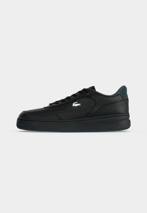 Basket basse noire avec design à lacets, talon texturé, semelle en caoutchouc et logo crocodile blanc sur le côté.