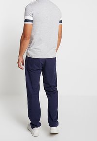 T-shirt gris à manches courtes avec des accents rayés bleu marine et blanc, associé à un pantalon large bleu foncé et des baskets blanches.