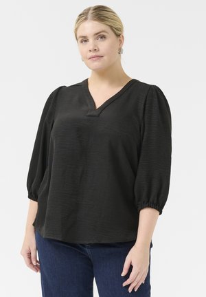 Black blouse with a V-neck, puffed sleeves, and textural fabric. Paired with blue jeans, featured on a model against a plain background.