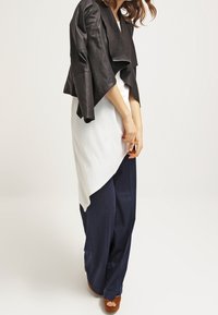 Black leather asymmetric jacket with a draped front, paired with a white tunic and navy wide-leg pants. Brown platform heels visible.