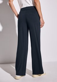 Breda byxor i mjukt marinblått tyg, med hög midja. Enkelt design med en slät textur och subtil rörelse.