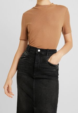 Hnědý krátký rukáv spojený s černou džínovou sukní s vysokým pasem. Sukně má přední kapsy a texturovaný povrch.