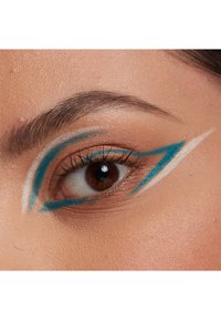 Blå och vit eyeliner konst visar skarpa geometriska mönster på ögonlocket, vilket kontrasterar med den naturliga hudtonen och den mörkbruna iris.