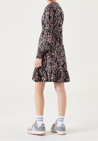 Sukienka w kwiaty z długimi rękawami, czarne tło, różowe i niebieskie kwiaty, falbaniasty dół, zestawiona z szarymi trampkami i paskowanymi skarpetkami.