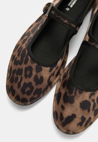 Ballerines en imprimé léopard avec une texture douce et veloutée, des bordures élastiques noires et une sangle sécurisée. Bout rond et construction flexible.