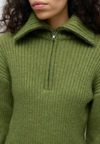 Maglione verde oliva con una texture a coste, colletto alto e design con zip a quarto. Presenta un tessuto spesso e caldo con dettagli a coste orizzontali.