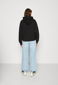 Svart kort hoodie med dragsko i huvan, ihop med ljusblå vida jeans och vita sneakers med svarta och grå accenter.
