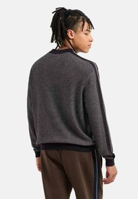 Maglione lavorato a maglia di colore grigio scuro con un motivo testurizzato, polsini e orlo a coste, e strisce laterali a contrasto sulle maniche.