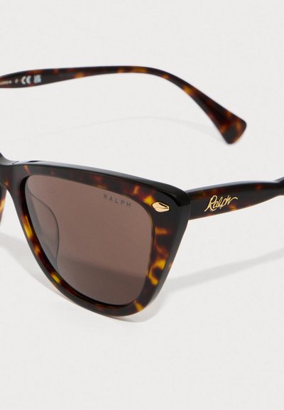 Ochelari de soare cu model tortoiseshell, design geometric cu ochi de pisică, lentile de culoare maro închis și branding auriu "Ralph" pe temple.