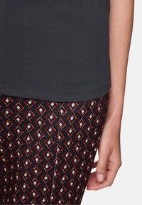 Dunkelgraues Baumwoll-T-Shirt mit kurzen Ärmeln, kombiniert mit schwarzen Hosen, die ein rotes, weißes und blaues geometrisches Rautenmuster aufweisen.