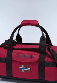 Sac de sport rouge avec des poignées noires, arborant un écusson avec le drapeau norvégien, un texte logo et une finition texturée. Design compact avec des poignées robustes.
