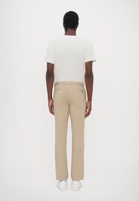 Béžové kalhoty slim fit s hladkou texturou a zadními kapsami, doplněné o bílé tričko s krátkým rukávem a bílé tenisky.