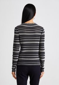 Schwarz-weißer gestreifter Langarmtop mit strukturiertem Strickdesign, das abwechselnd Linien zeigt und einen runden Ausschnitt hat, in schmaler Passform.