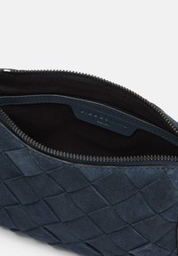 Niebieska skórzana torba o plecionej fakturze, z zamkiem błyskawicznym i miękkim czarnym wykończeniem. Wnętrze z widoczną metką markową wzdłuż krawędzi.