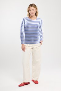 Langærmet hvid top med blå vandrette striber, parret med kremfarvede bukser og røde, strukturerede flade sko. Simpelt, afslappet design.