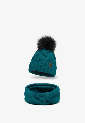 Teal gebreide beanie met een zwarte nepbont pompon en een bijpassende infinity sjaal, beide met een gemêleerd patroon en ribbelafwerking.