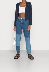 Námořnický zkrácený blazer, bílý crop top, světle a tmavě modré džíny s patchworkem, hnědé sandály a malá bílá kabelka.