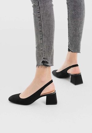 Czarne czółenka na obcasie typu slingback wykonane z gładkiego materiału, z noskiem w szpic i kwadratowym obcasem, zestawione z szarymi obcisłymi dżinsami.