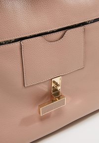 Ljusrosa läderhandväska med en jämn textur, iögonfallande rektangulär klaff, detaljer i guldton och en stilren låsförslutning.