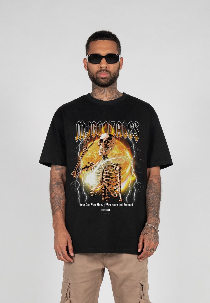 Sort grafisk t-shirt med et skeletdesign i orange og gule elementer, lynakcenter og fed tekst. Korte ærmer og afslappet pasform.