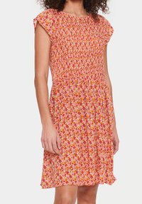 Kukallinen mekko, joka on valmistettu kevyestä kankaasta. Siinä on rypistetty yläosa, lyhyet liidinkainalohihat ja polveen ulottuva hame, jossa on monivärinen kukkakuosi.