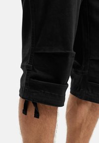 Sorte shorts med oppbrettede ermer laget av blandingsmateriale med bomull, med sidelommer og snøring i kanten for justerbarhet.