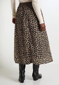 Falda midi de estampado de leopardo en color marrón y negro, con cintura fruncida y diseño fluido, combinada con botas de tacón negras.