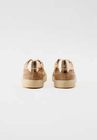 Brune semskete sneakers med metalliske gulldetaljer på hælene. Har en glat overflade, rund form og en beige gummisål.