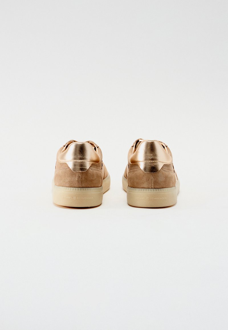 Sneakers in suede marrone con inserti metallici dorati sul tallone. Presentano una texture liscia, una forma arrotondata e una suola in gomma beige.