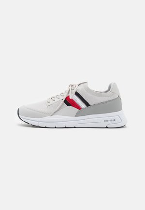 Sneaker grigio chiaro con una tomaia in maglia testurizzata, caratterizzata da una striscia di design rossa e blu navy. Suola in gomma con accentuazioni bianche e grigie. Logo del marchio sul tallone.
