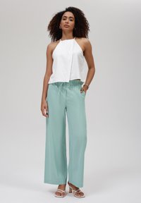 Top blanco sin mangas con un diseño drapeado, combinado con pantalones de pierna ancha verde claro que cuentan con una cinturilla elástica y bolsillos laterales.